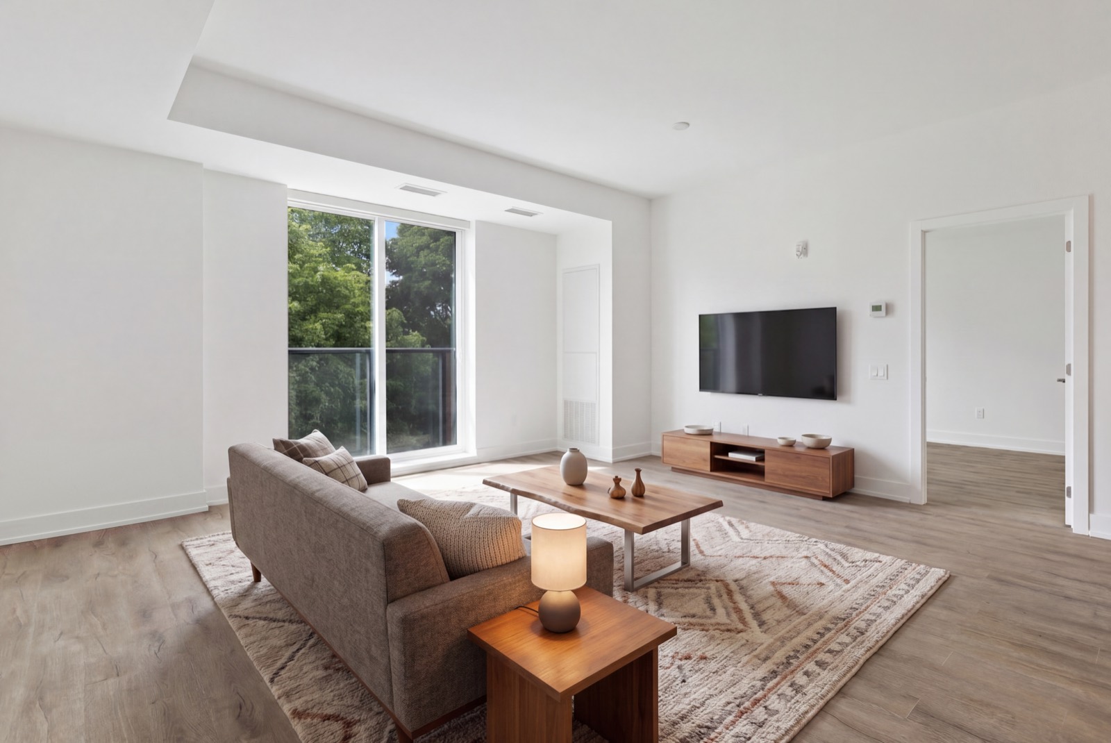 Living room staged with a grey sofa, walnut coffee table, patterned rug and a walnut TV console, seen from the doorway